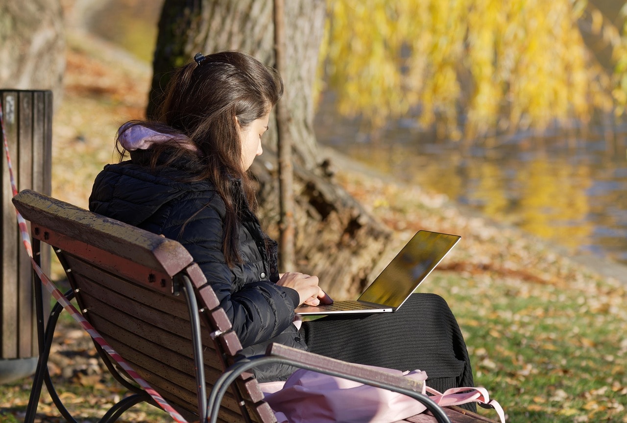A stock image of a young woman sitting on a bench with a laptop open on her lap. This is to illustrate the article teaching how freelance writers earn up to $300 per published poem